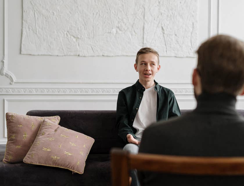 School social worker having a conversation with a male student sitting on the couch