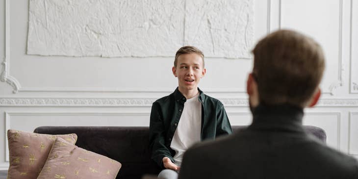 School social worker having a conversation with a male student sitting on the couch