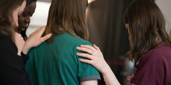 A service coordinator holding her client's shoulder and showing something to her while her support group looks on.