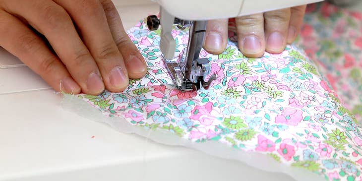 close up view of a sewing machine operator sewing a protective mask