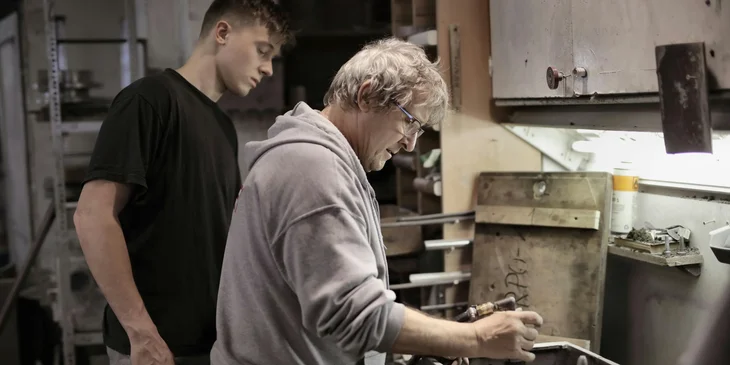 A shop foreman showing an apprentice how to operate a shop's machinery.