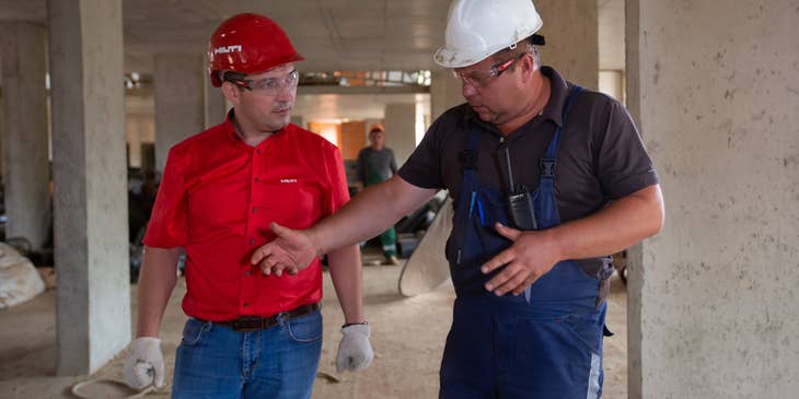 Site engineer wearing a hard hat and a pair of industrial gloves and listening to the updates of the foreman on the construction site