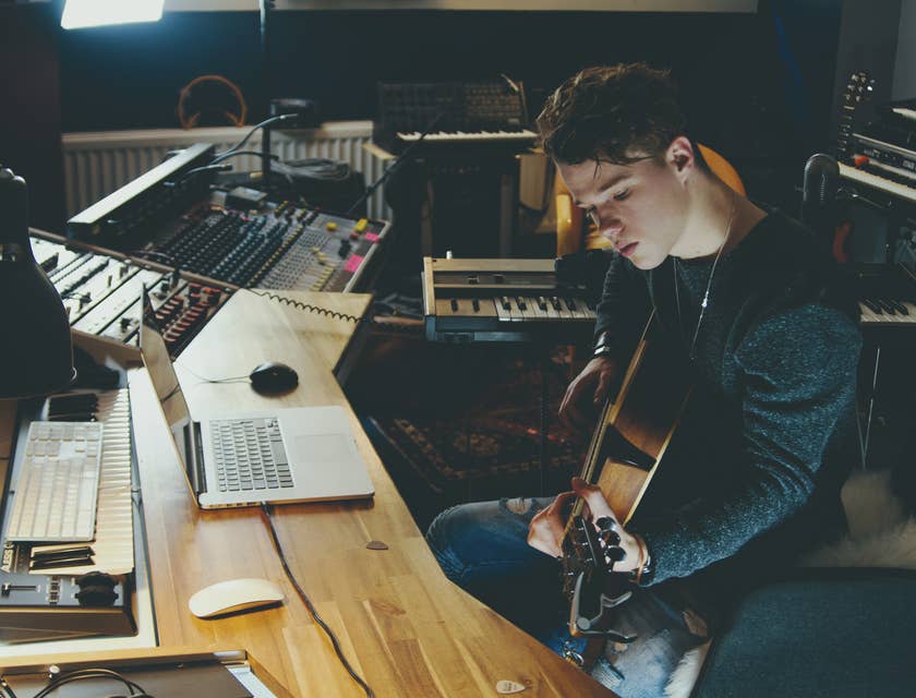 songwriter working in a studio with a guitar and laptop