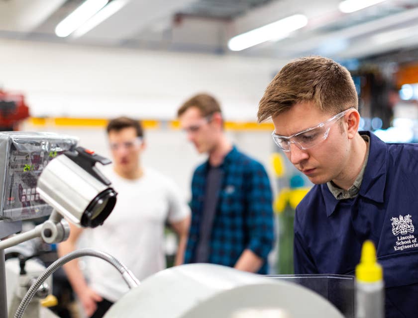 Staff engineer wearing protective goggles while putting together the manufactured product in a laboratory with his colleagues on the background