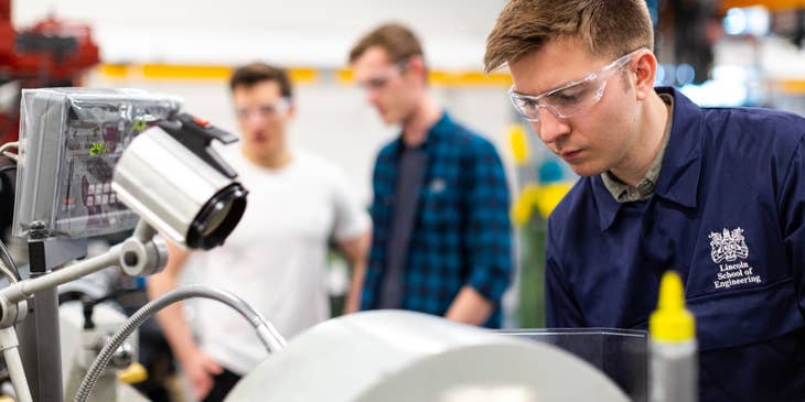 Staff Engineer wearing protective goggles while putting together the manufactured product in a laboratory with his colleagues on the background