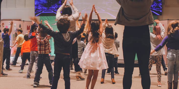 Sunday school teacher teaching students a dance of praise while viewing in a large screen