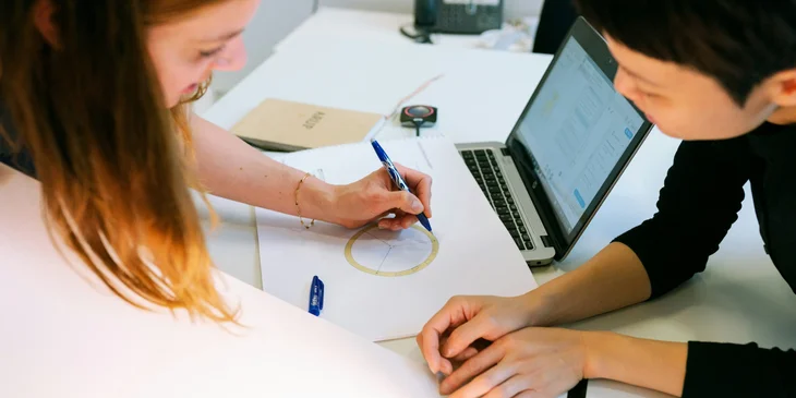 A female supply chain engineer writing her ideas for a new inventory management proposal while her coworker looks on.