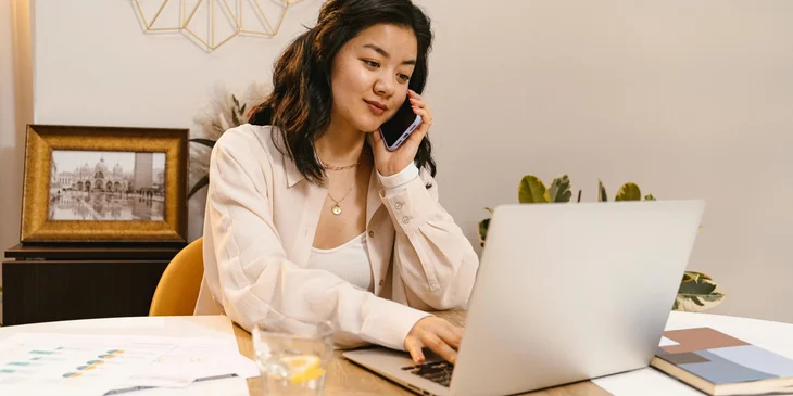 A tax accountant prepares a tax return report on a laptop while talking to someone on a mobile phone.