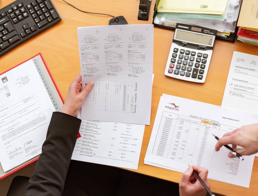 photo of one person holding a paper on his left hand and pen on the other hand while the other person is pointing out something on the desk