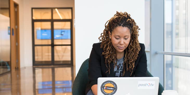 A female technical recruiter sitting on a black chair working on her laptop with a cup of coffee.