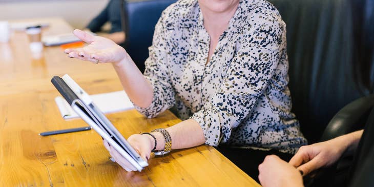 A female technical sourcer showing a notebook and having a conversation with a colleague..