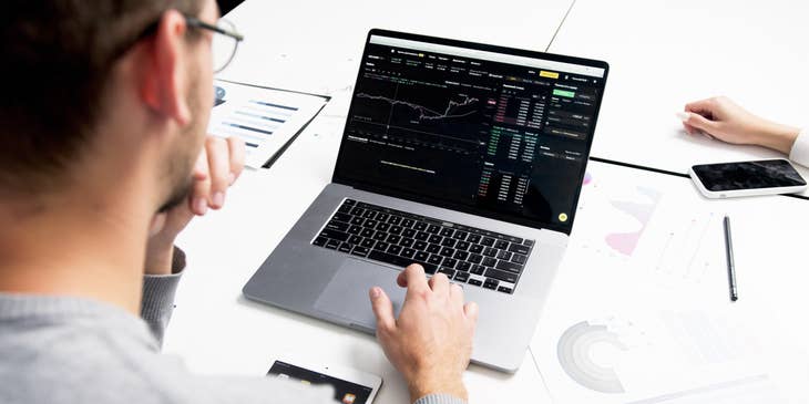 Trader wearing eyeglasses while looking at a real-time report on his laptop
