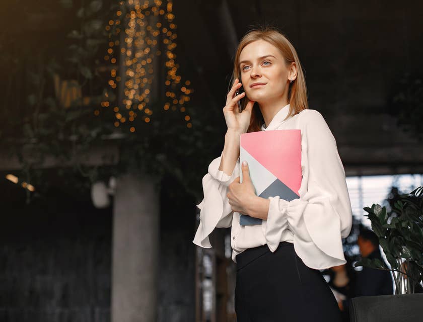 female transaction manager holding a portfolio folder on one hand while using her mobile phone