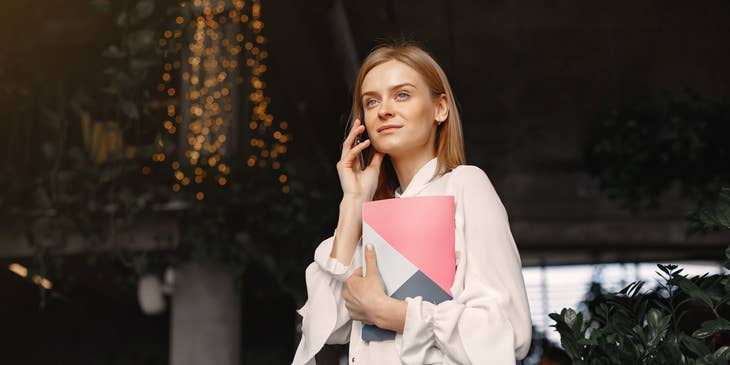 female Transaction Manager holding a portfolio folder on one hand while using her mobile phone
