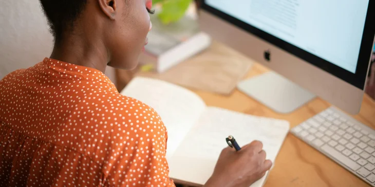 A transition manager writing in a notebook at a desk with a computer.