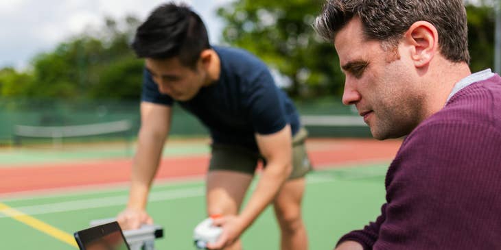 Validation engineer analyzing the test results of a new product with the help of his assistant in a tennis court