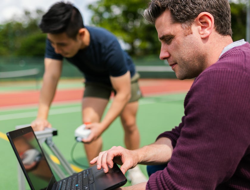 Validation engineer analyzing the test results of a new product with the help of his assistant in a tennis court
