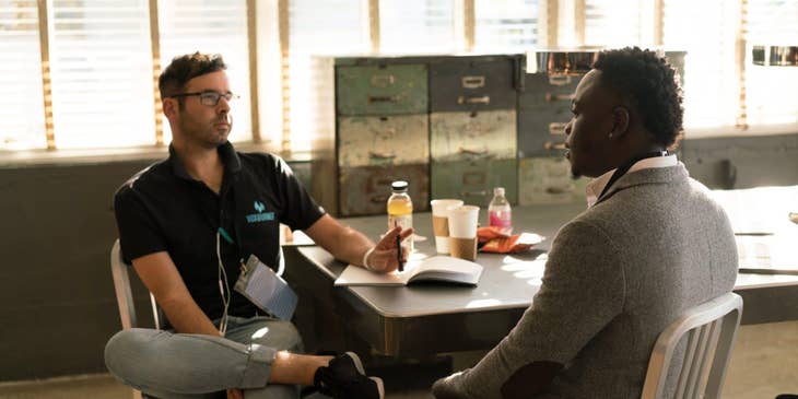 male victim advocate wearing glasses and sitting on the table while holding a pen and having a dialogue with his client