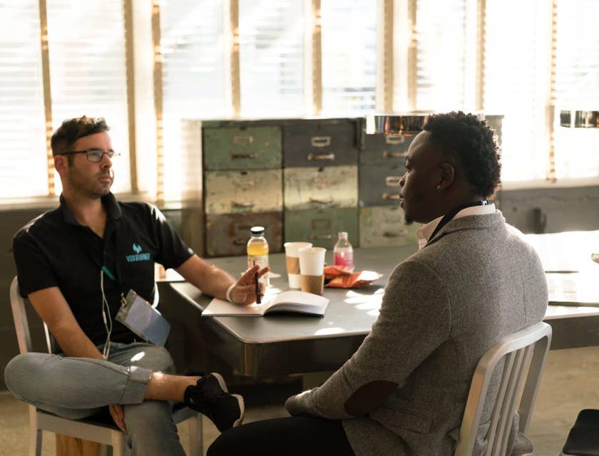 male victim advocate wearing glasses and sitting on the table while holding a pen and having a dialogue with his client