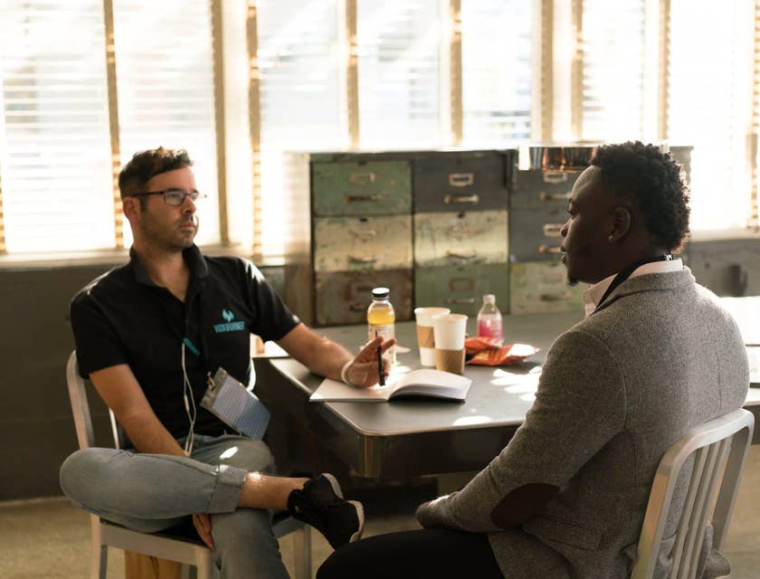 male Victim Advocate wearing glasses and sitting on the table while holding a pen and having a dialogue with his client