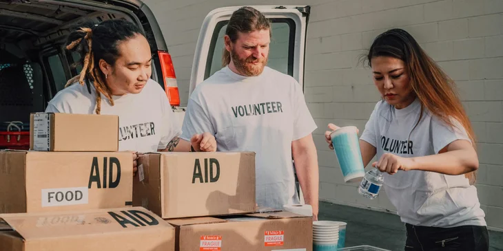 Three volunteers distributing boxes of aid supplies in their local community.