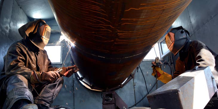 a welder and his helper working on a steel pipe