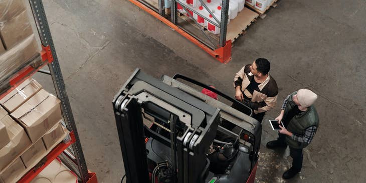 A yard jockey inside a warehouse beside a manager and about to transport equipment to be used for loading.