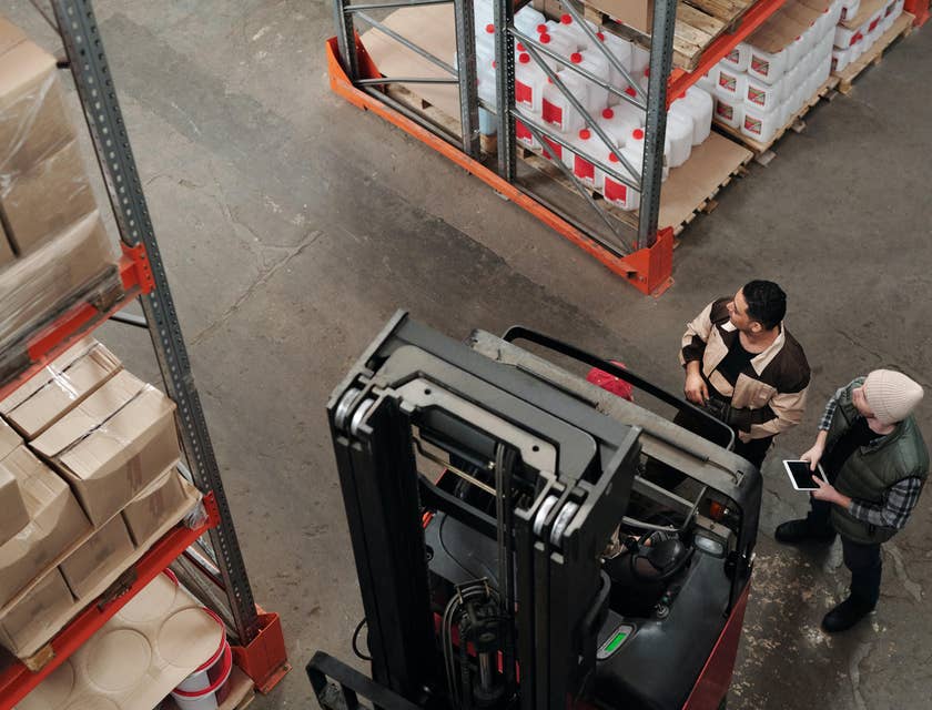 A yard jockey inside a warehouse beside a manager and about to transport equipment to be used for loading.